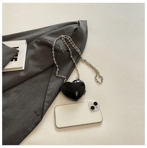 Macro view of a black heart-shaped acrylic mini bag with a silver chain on a gray blazer