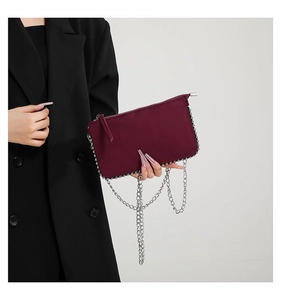 Detail of burgundy shoulder bag with silver bead trim and metallic chain on a black blazer