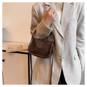 Retro brown suede half-moon shoulder bag styled with a plaid blazer for a minimalist aesthetic