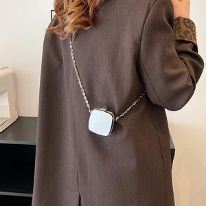 Silver metallic mini square crossbody bag with fine chain strap shown on a brown blazer