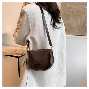 Detail of dark brown matte saddle bag with gold zippers and adjustable shoulder strap