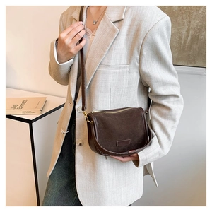 Detail of the brown suede saddle bag showing its matte texture and golden buckle on grey suit