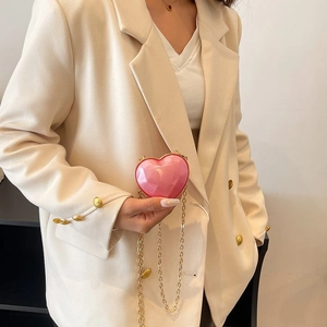 Detail of pink heart-shaped acrylic mini bag with gold chain on white blazer