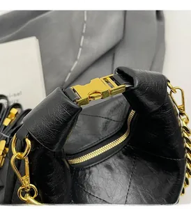 Detail of black pleated leather handbag featuring gold metal buckle and chain strap