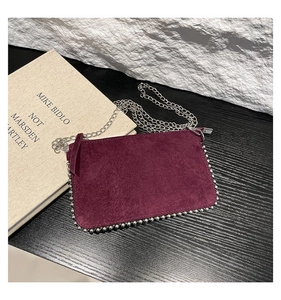 Macro view of burgundy suede shoulder bag featuring silver bead trim and chain strap