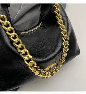 Detail of black pleated leather handbag with bold gold metal chain and textured finish