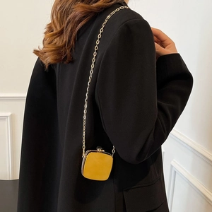 Close-up of bright yellow mini square bag with gold chain strap on black suit