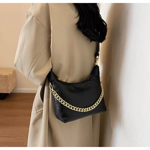 Close-up of black quilted dumpling bag featuring a bold gold chain and leather shoulder strap