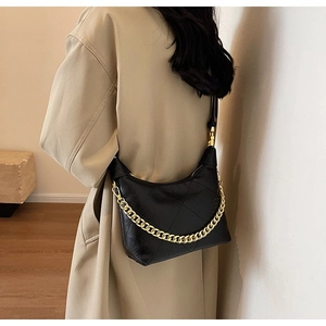 Detail of black quilted dumpling bag featuring a bold gold chain strap and glossy finish