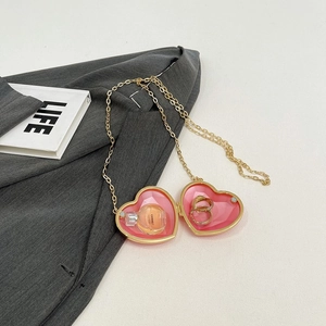 Pink heart-shaped acrylic mini bag with gold chain shown holding a ring and perfume