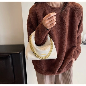 Detail of white quilted crescent handbag with chunky gold chain strap on model