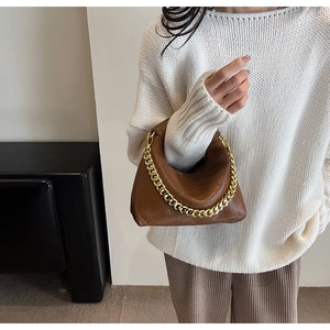 Detail of brown quilted hobo bag with chunky gold chain handle on a model in white knitwear