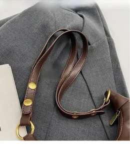 Détail de la bandoulière réglable avec boucles dorées sur un sac vintage en cuir marron