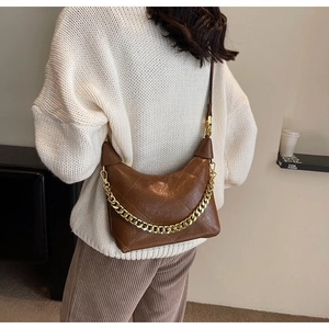 Close-up of brown quilted faux leather dumpling bag with chunky gold chain decoration