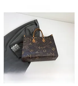 Top view of large dark brown tote bag with letter print and metal rings on a white surface
