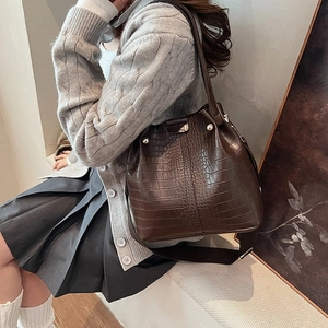 Detail of dark brown croc-embossed bucket bag with gold rivets and wide textile strap