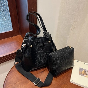 Detail of black crocodile texture bucket bag with gold studs and wide canvas strap