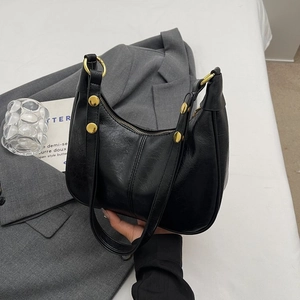 Détail d'un sac porté épaule en similicuir noir avec rivets dorés et fermeture zippée chic
