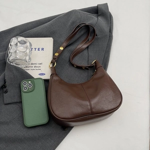 Détail du sac demi-lune en cuir marron foncé avec texture grainée et bandoulière