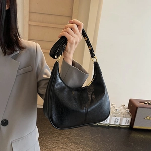 Détail du sac demi-lune noir avec garniture dorée porté par un mannequin en veste grise