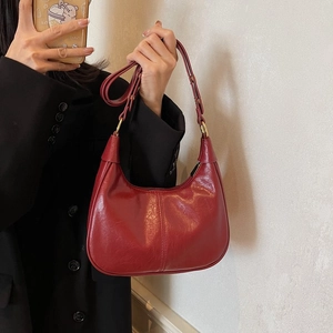 Détail d'un sac porté épaule en cuir rouge brillant avec bandoulière réglable et boucle d'or