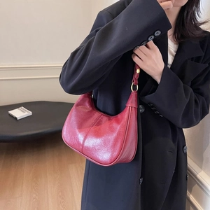 Détail d'un sac demi-lune en cuir ciré rouge avec anneaux dorés sur un blazer noir