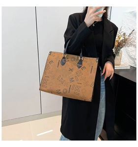 Detail of a large brown leather tote bag with letter print and blue top handles