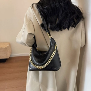 Chic black quilted dumpling bag with gold chain strap, worn as a stylish underarm bag