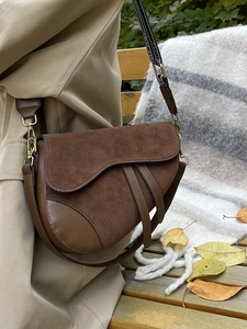 Detail of a brown leather saddle bag with wide logo strap and vintage gold hardware