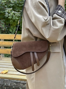 Detail of a dark brown suede saddle bag featuring leather straps and vintage gold hardware