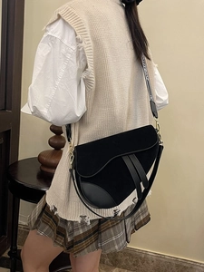 Detail of black saddle bag with textured jacquard strap worn by a model in casual outfit