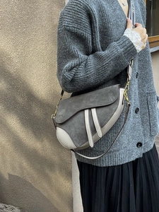 Detail of grey suede saddle bag with branded shoulder strap and metal hardware