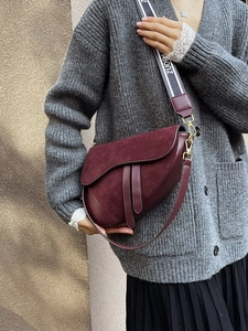 Detail of burgundy saddle bag with suede texture and wide graphic canvas shoulder strap