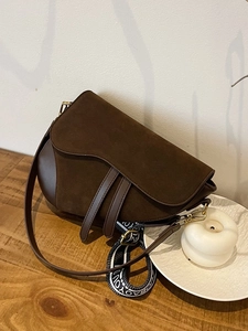 Detail of dark brown suede saddle bag with lettered jacquard wide strap and gold hardware