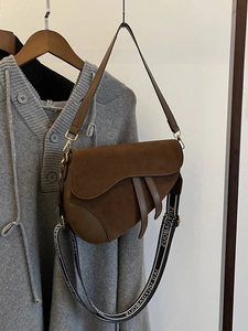 Detail of a brown suede saddle bag featuring a stylish wide patterned fabric shoulder strap