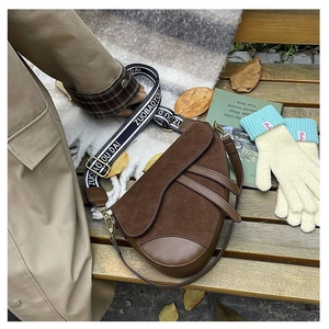 Detail of brown suede saddle bag with wide jacquard strap on a rustic wooden bench