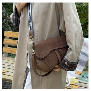 Detail of a brown suede and leather saddle bag with wide blue shoulder strap on a trench coat