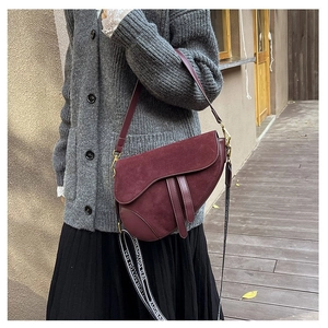 Detail of burgundy saddle bag with wide logo strap and smooth leather trim finish