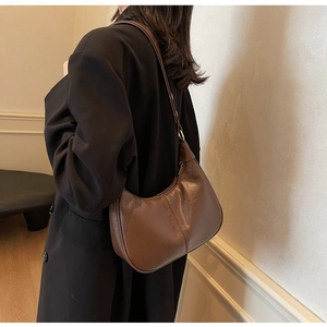 Sac hobo en cuir marron avec coutures apparentes porté par un mannequin en manteau noir