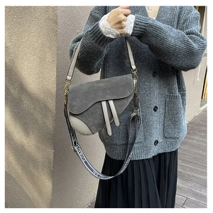 Macro view of grey suede saddle bag with wide patterned strap and metal buckle detail
