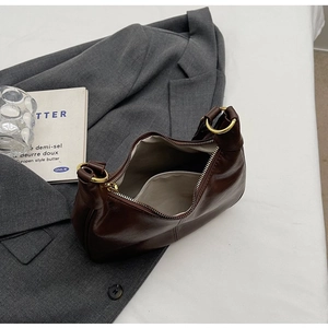 Sac hobo classique en cuir marron foncé avec anneaux dorés posé sur un blazer