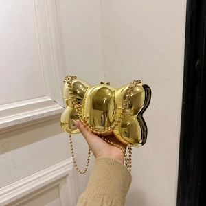 Vue détaillée d'une pochette dorée en forme de nœud avec bandoulière à perles tenue à la main