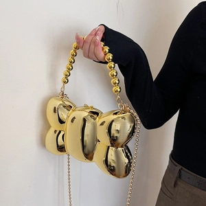 Détail d'un sac à main doré en forme de ballon avec une poignée élégante en perles