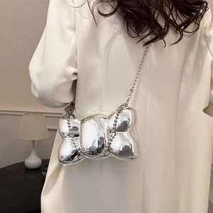 Sac bandoulière argenté en forme de nœud 3D porté sur un blazer blanc élégant