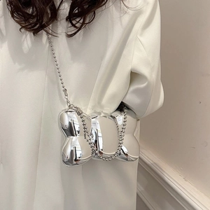 Sac bandoulière argenté en forme de nœud avec chaîne à perles sur blazer blanc