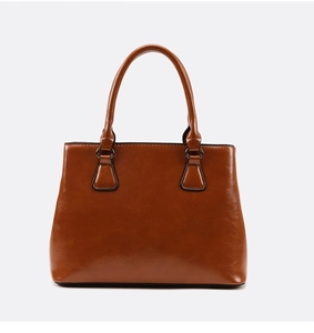Detail of caramel brown glossy leather tote bag with sturdy double handles and metal hardware