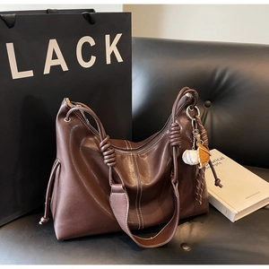 Detail of dark brown leather tote featuring contrast stitching and decorative knotted strap