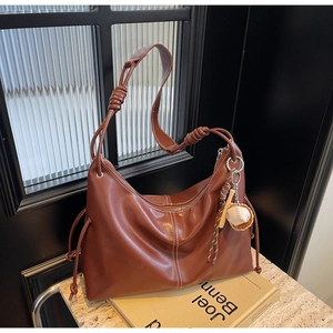 Detail of brown leather tote bag with spiral knot strap and baseball charm on books
