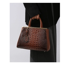 Detail view of brown crocodile texture leather handbag with gold metal bar closure