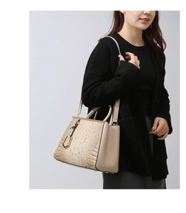 Detail of beige faux crocodile leather handbag with elegant top handle and gold hardware